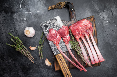 Fresh uncooked lamb chops and ribs with thyme on cutting board dark textured background overhead meat preparationの写真素材