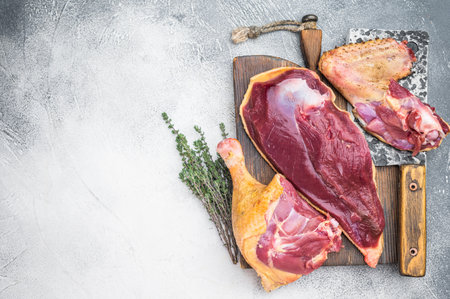 Raw duck meat cuts with breast and leg on wooden board with knife and thyme. Gamebird poultry game meat on gray background copy space.の写真素材