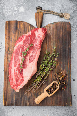 Raw beef chuck eye steak with rich marbling on wooden board with thyme and pepper. Fresh beef cut overhead with copy space.の写真素材