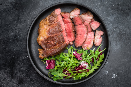 Pan fried beef chuckeye roll steak sliced and served with leafy greens. Gourmet beef dish with copy space top view.の写真素材