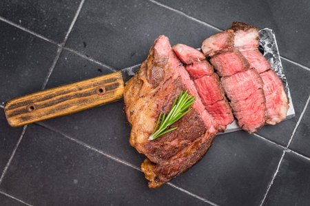 Grilled and Sliced beef chuck eye roll steak cooked medium rare on meat cleaver with rosemary on dark tile background with copy space.の写真素材