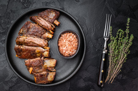 Sliced BBQ roasted lamb breast ribs on black plate with salt and fork dark stone background barbecue meat copy space.の写真素材