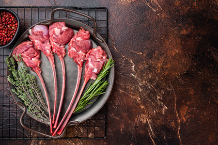 Raw lamb cutlets on bone in cast iron skillet with herbs warm dark background top view butcher meat copy spaceの写真素材