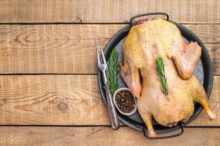Raw whole goose on pan with rosemary and pepper on wooden background top view. Poultry game meat ingredient with copy space.の写真素材