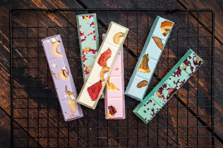 Variety of handmade gourmet chocolate bars with berry and nut toppings on metal grid dark wood...