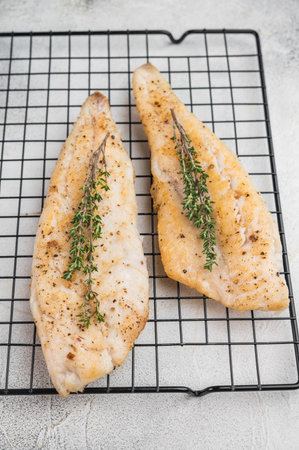 Roasted flaky whitefish fillets with fresh thyme, food photography on cooling rack over light stone...