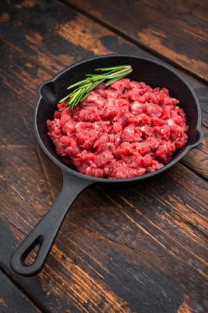 Raw chopped beef meat with herbs in black skillet over bright surface perfect for recipe design...