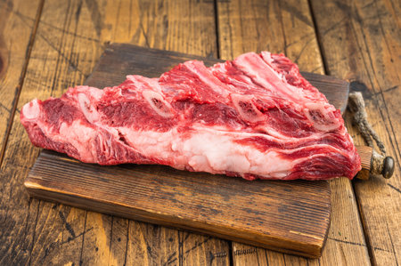 Fresh uncooked beef ribs slab with visible bones and herbs on cutting board. Wooden background for BBQ cooking and butchery conceptsの写真素材