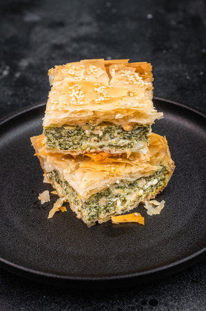 Traditional crispy phyllo pastry with spinach cheese filling cut into pieces, modern rustic presentation.の写真素材