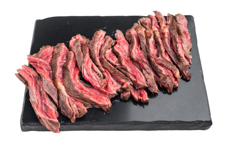 Medium rare grilled bavette flap steak sliced thin showing meat fibers and texture served on dark stone board isolated on white background.の写真素材