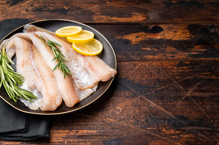 Organic Raw Haddock fish fillets, whitefish on a plate with herbs. wooden background. top view.