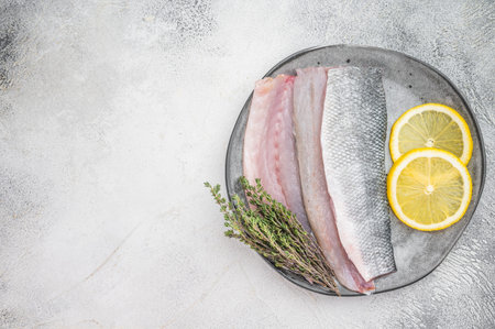 Raw sea bass fillet with skin served on plate with lemon and thyme, fresh Mediterranean seafood ingredient in minimal overhead food styling compositionの写真素材