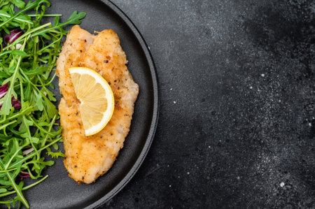 Pan fried red ocean perch fish fillet served with fresh arugula salad and lemon on dark background