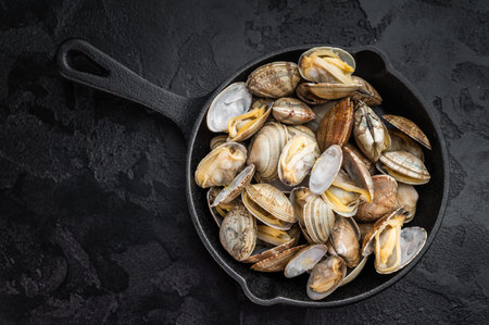 Prepared vongole mollusks served in skillet on textured black surface. Mediterranean seafood flat lay