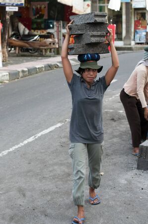 UBUD - 4 April 2011: woman working in construction carries very heavy stones on her head on April 4, 2011 on Ubud street on Bali, Indonesiaのeditorial素材