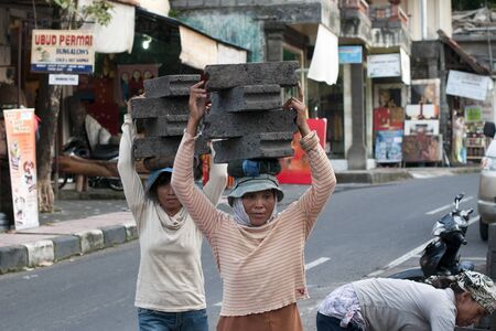 UBUD - 4 April 2011: woman working in construction carries very heavy stones on her head on April 4, 2011 on Ubud street on Bali, Indonesiaのeditorial素材