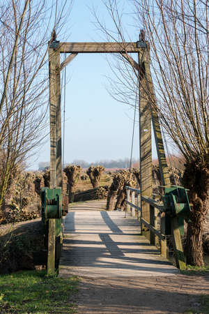 nature area in  holland with willows and  wooden drawbridge and small river