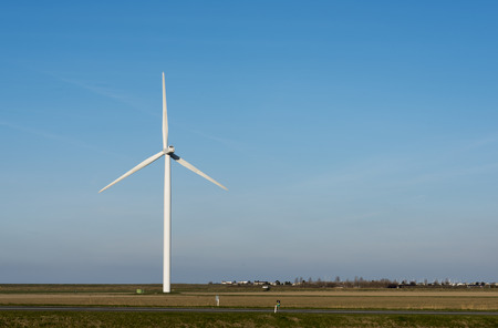 single white windmill with very blue summer sky and green farmland with farm on the background and...