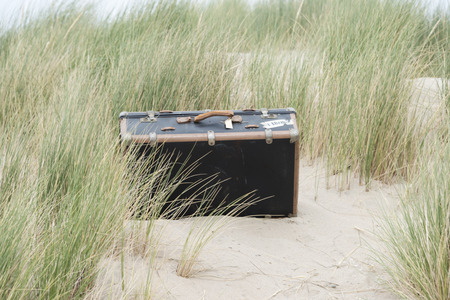 old leather used suitcase hidden in the sandy dunes near the beachの写真素材