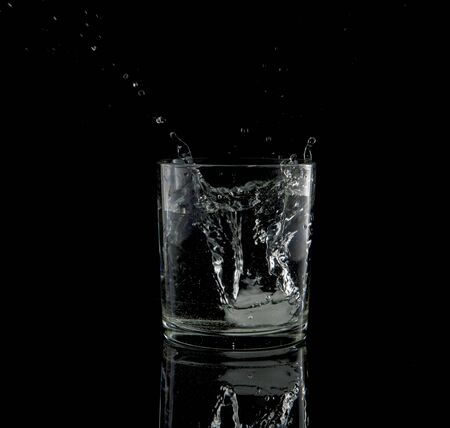 almost black and white of a splash from a falling ice cube in glass of waterの写真素材