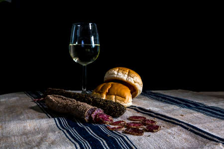 still life table with a glass of white wine assorted dry sausages and bread on a flour cloth with blue stripesの写真素材