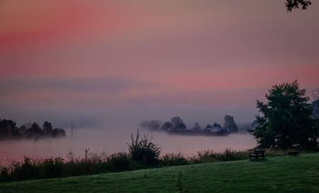 ship in the maas during sunrise in the early morning in limburg in holland with the trees mist and hazy fogの写真素材