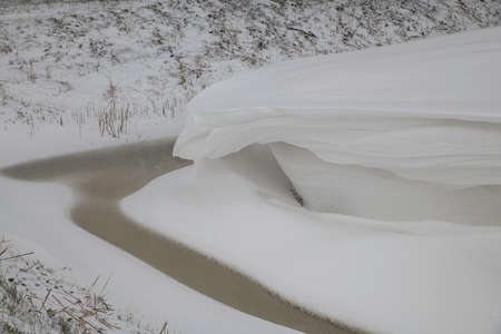 a thick layer of snow overhanging an almost frozen ditch during the winte rin hollandの写真素材