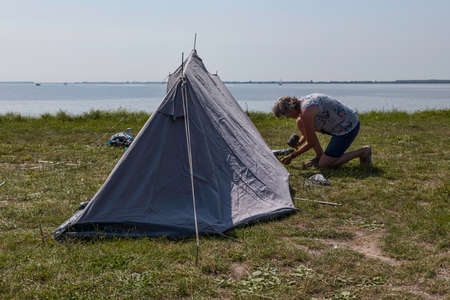 woman setting up a tent at the waterlineの写真素材