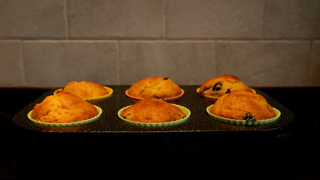 muffins or cupcakes with blueberries in muffin tins with the kitchen tiles in the backgroundの写真素材