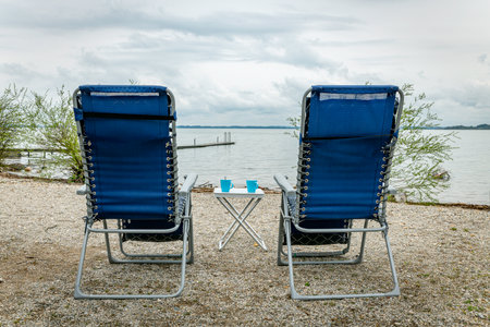 two camping chairs on a gravel beach overlooking the water and a wooden deckの写真素材