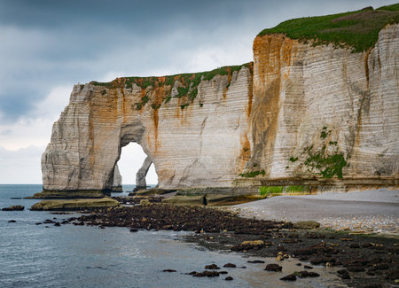 Landscape photo of tall, steep limestone cliffs by the ocean with one with a hole in it creating an arch view from the beachの写真素材