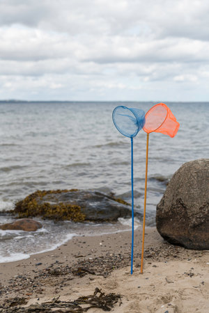 an orange and a blue fishing net on a pole standing on the beach with the sea and the horizon as a background in natureの写真素材