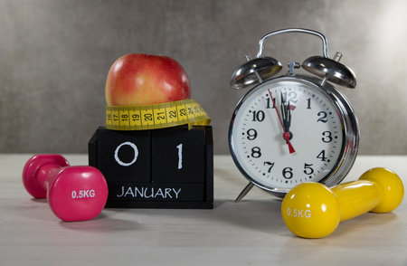 A composition symbolizing New Years resolutions with dumbbells, an apple, a tape measure, and a clock. Ideal for illustrating fitness goals and healthy lifestyles.の写真素材