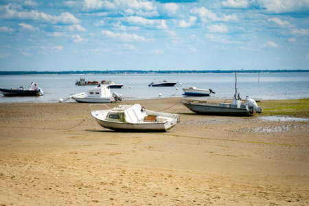 Several small boats rest on a sandy beach during low tide, surrounded by calm waters and a serene atmosphere. This picturesque seaside scene captures tranquility on the Atlantic coast of France near Bordeauxの写真素材