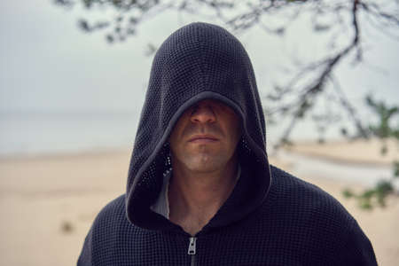 A person in a black hoodie looks like assassin. Cosplay. Sea shoe at the background. High quality photoの写真素材