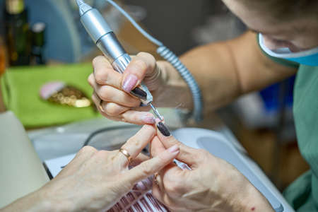 Woman in nail salon receiving manicure in beauty salon by beautician who use electric nail file drill with burst flying dust and debris around. Concept of nail care.の写真素材