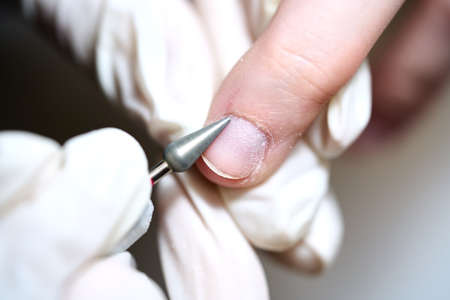 Woman in nail salon receiving manicure in beauty salon by beautician who use electric nail file...