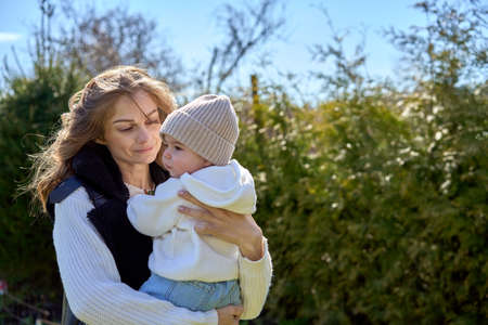 Mother holding shes daughter on the hands and looking at her with love and smile. Baby in the cap and hoodieの写真素材