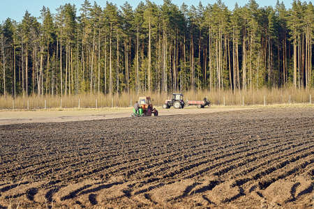 The tractor plows the field, cultivates the soil for sowing grain. Farmer standing behind the tractor during process. The concept of agriculture and agricultural machinery.の写真素材