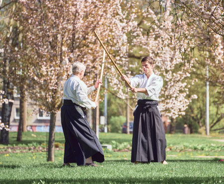 Riga, Latvia - May 8, 2022: Two aikido fighters training with stick in the public park. Blooming sakura at the background.のeditorial素材