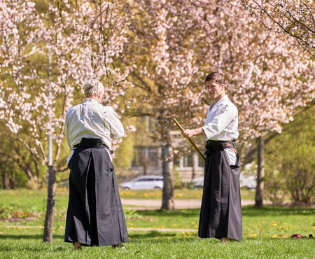 Riga, Latvia - May 8, 2022: Two aikido fighters training with stick in the public park. Blooming sakura at the background.のeditorial素材