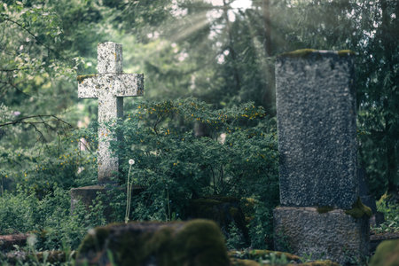 In this peaceful and tranquil cemetery, an ornate cross stands tall amidst the lush greenery and dappled sunlightの写真素材