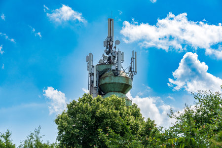 A contemporary telecommunication tower stands tall among flourishing trees beneath a beautifully clear blue skyの写真素材