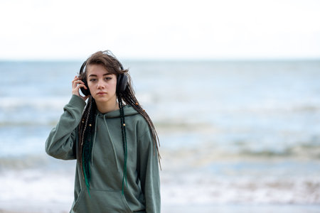 Close-up of teenager girl with dreadlocks listening to music with headphones on the seashore during the daytime.の写真素材