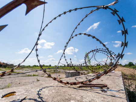 A closeup view of old, rusty barbed wire spiraling underneath a bright blue sky in a vast, desolate landscapeの写真素材