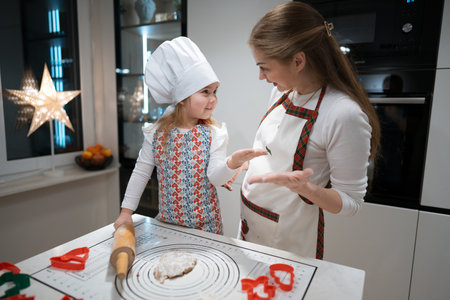 A joyful moment for a mother and daughter happily baking cookies together in a warm, loving kitchenの写真素材