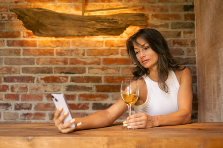 In a cozy and rustic interior, a stylish woman elegantly sips on her wine while capturing the moment...