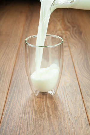 Healthy breakfast milk from a jug in a glass on a wooden table splashes of milk.の写真素材