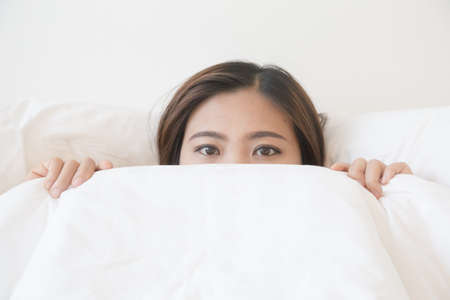 asian woman lying in bed under blanketの写真素材
