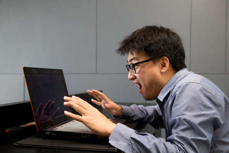 Asian man surprised with laptop computer looking at screen excited and happyの写真素材